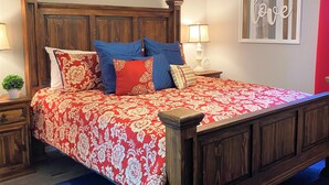 Een slaapkamer met een houten bed, een plafondventilator, een bloemenbedekking rood en wit, en een bord met daarop de tekst 'blessed'.