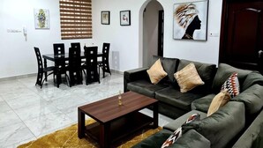 Ein Wohnzimmer mit einem dunkelgrünen Sofa, einem Holztisch und einem Essbereich mit einem schwarzen Tisch und Stühlen.
