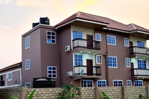 A multi-story residential building with balconies, air conditioning units, and a stone wall in the foreground.