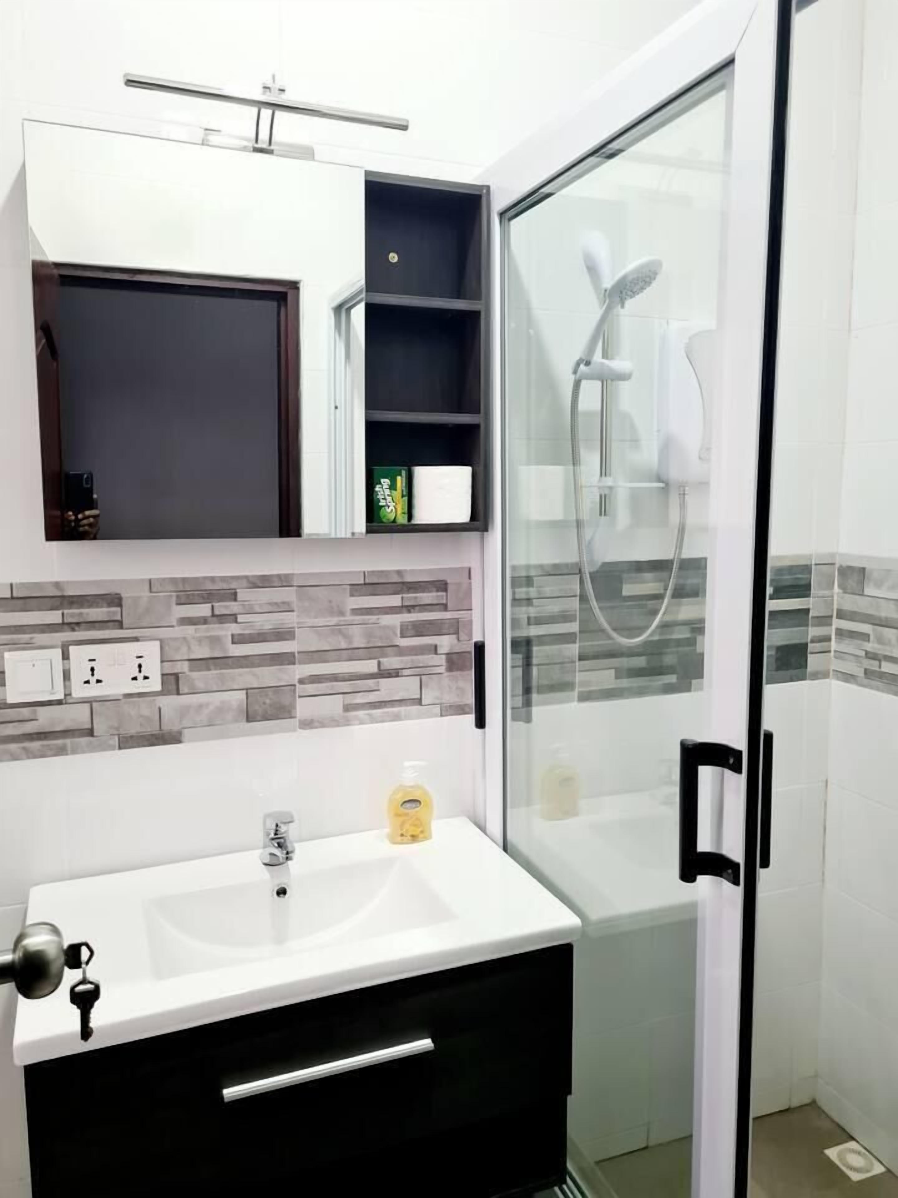A bathroom with a white sink, a mirror, a shower with a glass door, and a tiled wall.