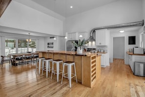 Een ruime keuken met een centraal eiland, houten vloeren, witte kastjes en een groot raam voor natuurlijk licht.