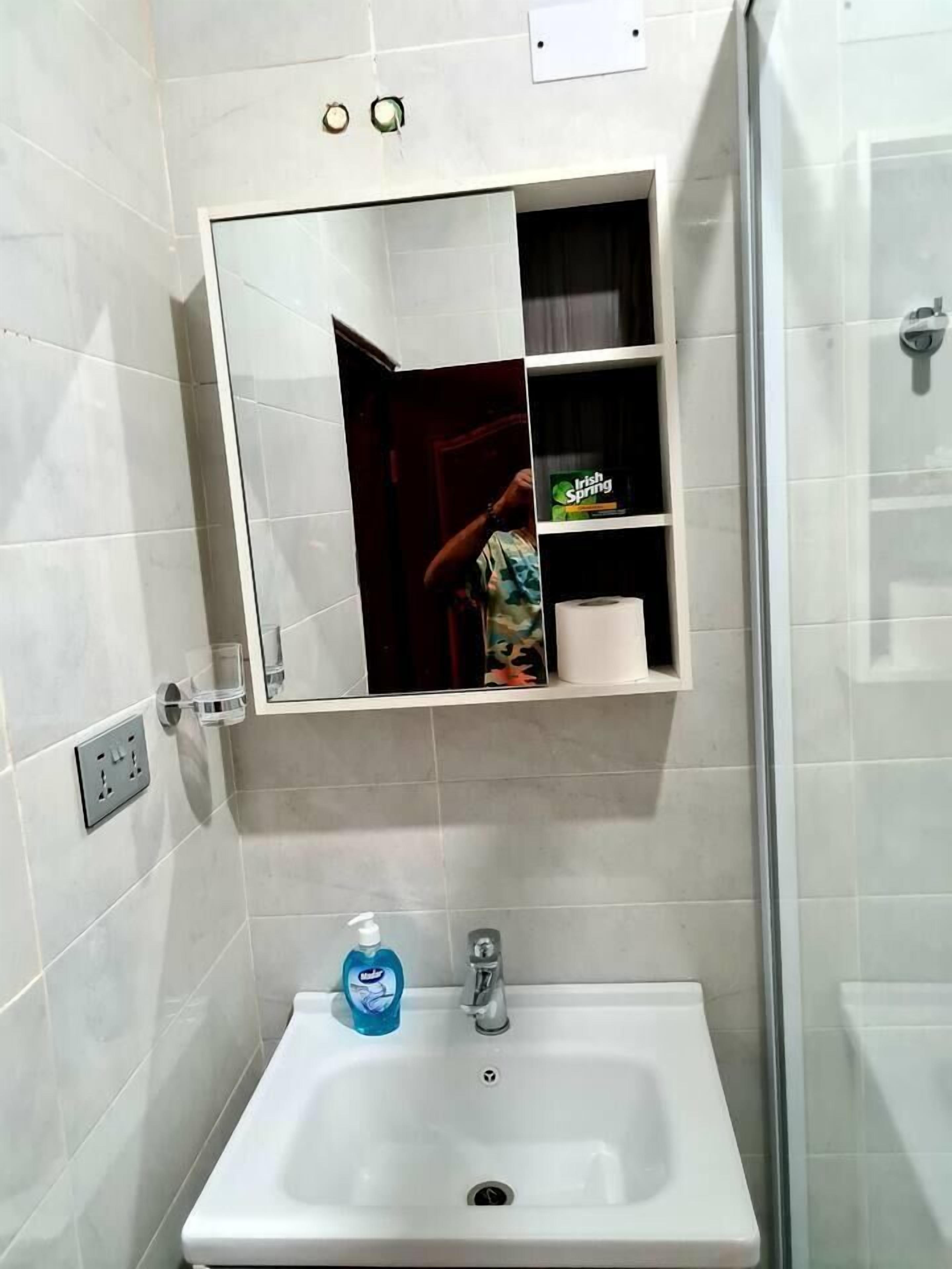 A bathroom with a white sink, a mirror, and a shelf with toiletries.