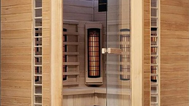 Een sauna met houten wanden, een glazen deur en planken met flessen.