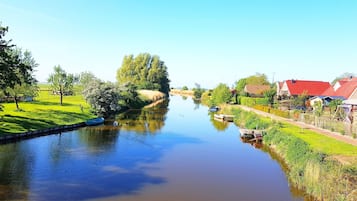A calm river with houses on the right bank and a tree-lined path on the left.