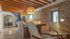 Un vaste espace dédié à la salle à manger, avec une table et des chaises en bois, des murs en pierre et un escalier menant à un niveau supérieur.