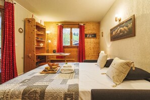 A cozy room with a bed, a wooden shelf, a table with a lamp, and a window with curtains.