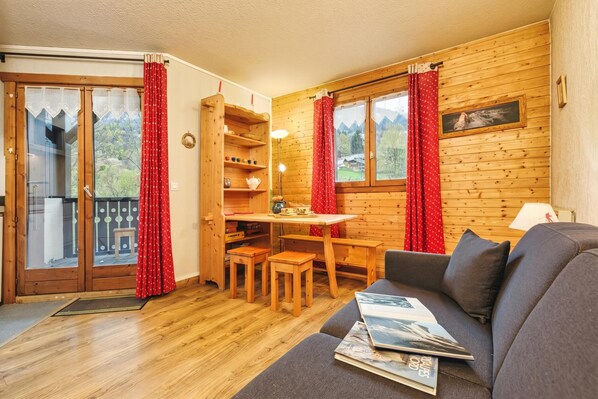 A cozy room with a wooden interior, a sofa, a table with chairs, and a view through the windows.