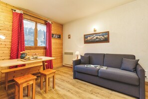 Une pièce chaleureuse aux murs en bois, avec une table à manger et des bancs, un canapé gris et une fenêtre ornée de rideaux rouges.