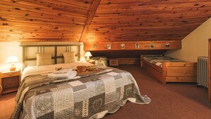 Una habitació acollidora amb sostre de fusta, un llit gran amb col·cha, una nitzeta, un armari i un fanal.