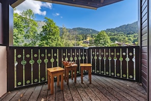 Une terrasse en bois avec deux tables et des chaises, une clôture décorative et une vue panoramique sur les montagnes.