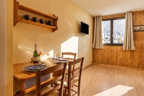 A dining area with a wooden table set for two, a television mounted on the wall, and a window with curtains. - Cham Sud G45 / 2-Min Walk to Centre, Chamonix, France (Chamonix)