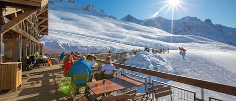Un terrazzo in legno con tavoli e sedie affacciato su un paesaggio montano innevato.