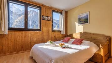 A bedroom with a wooden headboard, a bed with white linens, a window with a mountain view, and a framed picture on the wall.