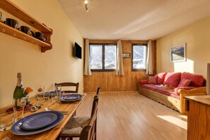 A cozy room with a wooden dining table set for two, a sofa with red cushions, and a large window with a view of snowy mountains. - Cham Sud G45 / 2-Min Walk to Centre, Chamonix, France (Chamonix)
