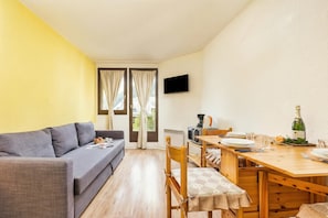 Una habitación con un sofá, una mesa de comedor con sillas, un televisor de pantalla plana en la pared y una ventana con cortinas.