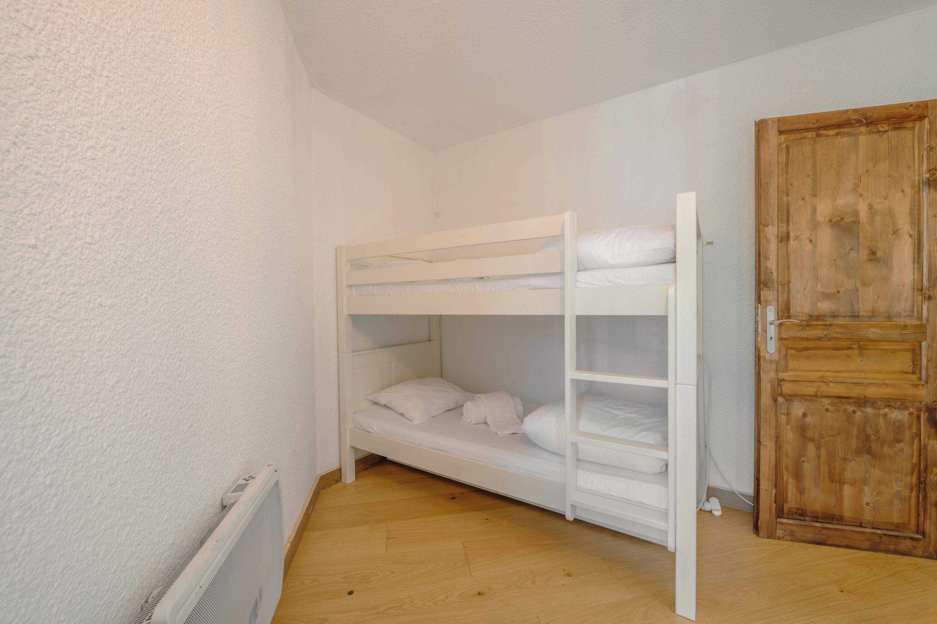 A bunk bed with white bedding in a room with wooden flooring and a wooden door.