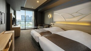 Une chambre d’hôtel avec deux lits, un bureau, une chaise, une télévision et une grande fenêtre donnant sur la ville.