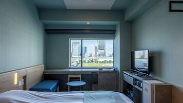 A hotel room with a bed, a desk, a chair, a TV, and a window with a city view.