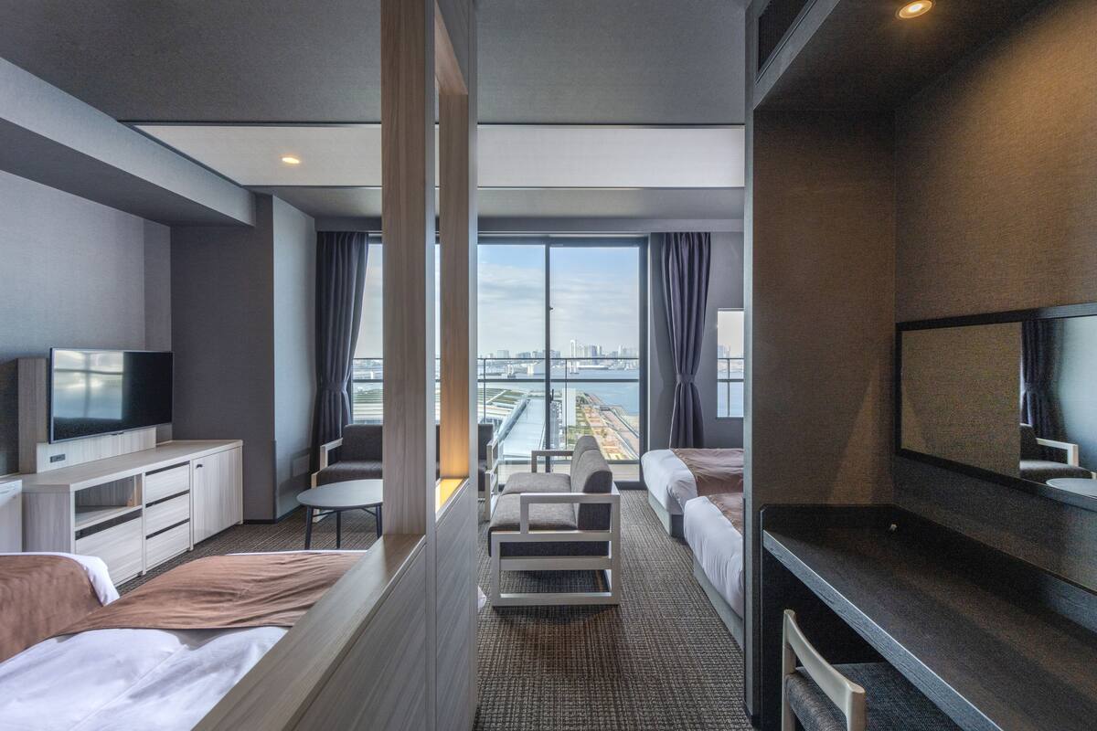 Una habitación de hotel moderna con un ventanal grande, una televisión de pantalla plana, un sofá, una cama y un escritorio con espejo.