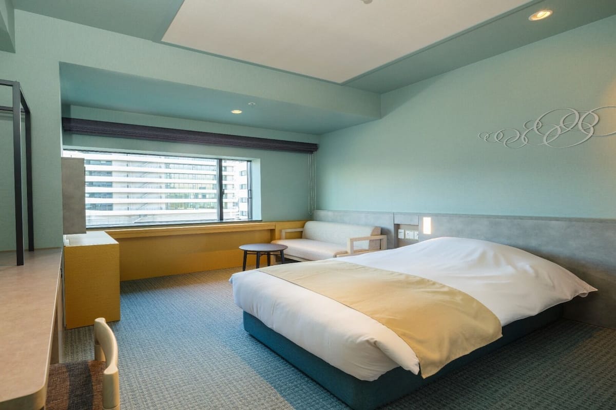 Habitación de hotel con cama, escritorio, silla, ventana con persianas y pared con diseño circular.