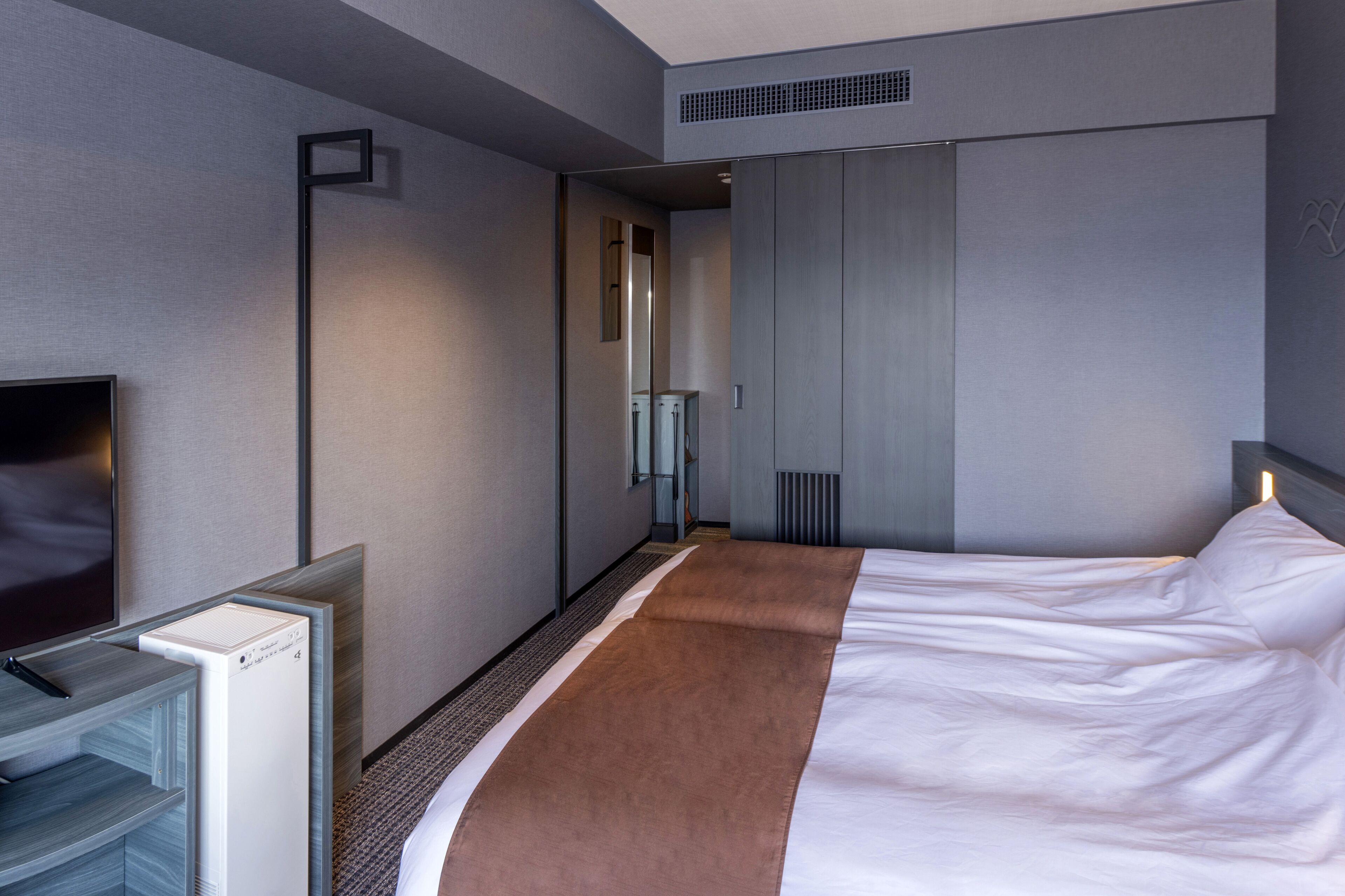 A modern hotel room with a large bed, a flat-screen TV, a minibar, and a walk-in closet.