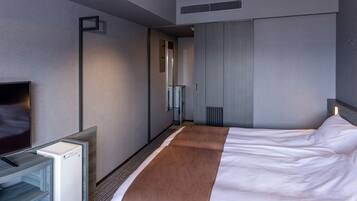 A modern hotel room with a large bed, a flat-screen TV, a minibar, and a walk-in closet.