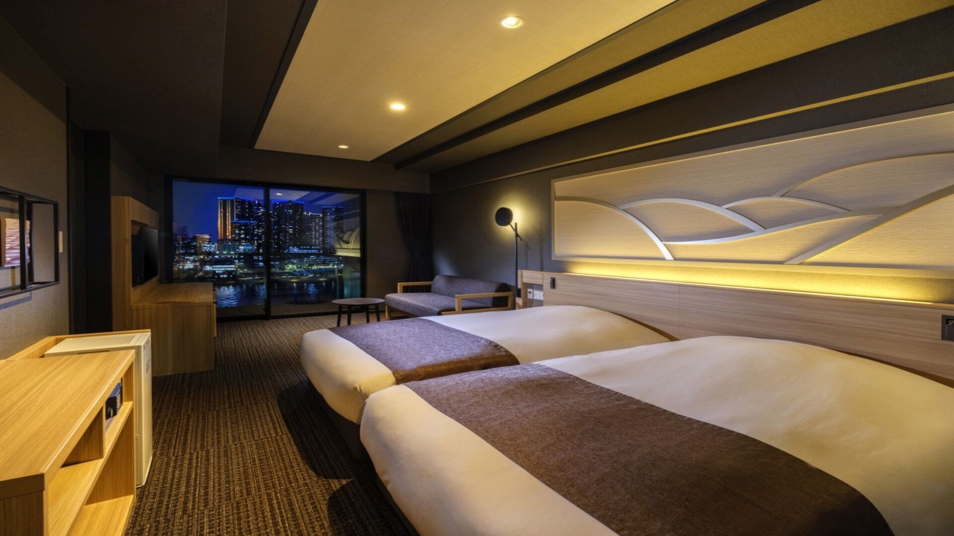 A hotel room with a city view, two beds, a desk, and a chair.