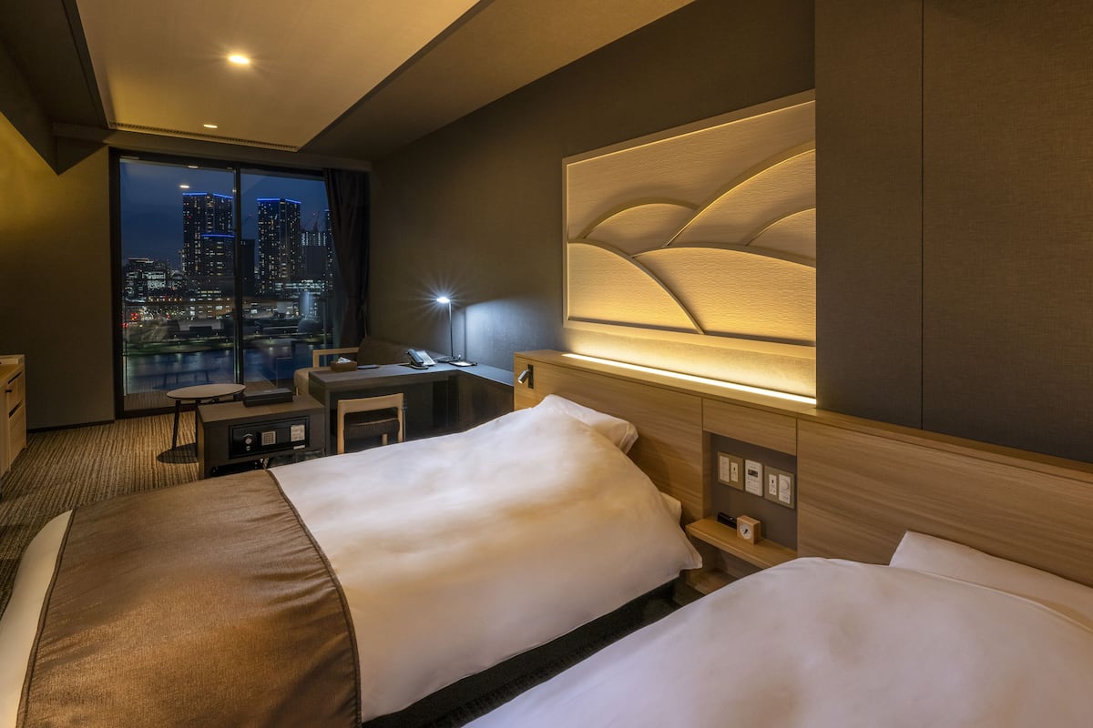 Habitación de hotel con una cama grande, un escritorio y vista a la ciudad de noche.