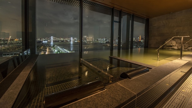 Une piscine intérieure moderne offrant une vue sur la ville, avec un mur de verre et un mur en pierre.