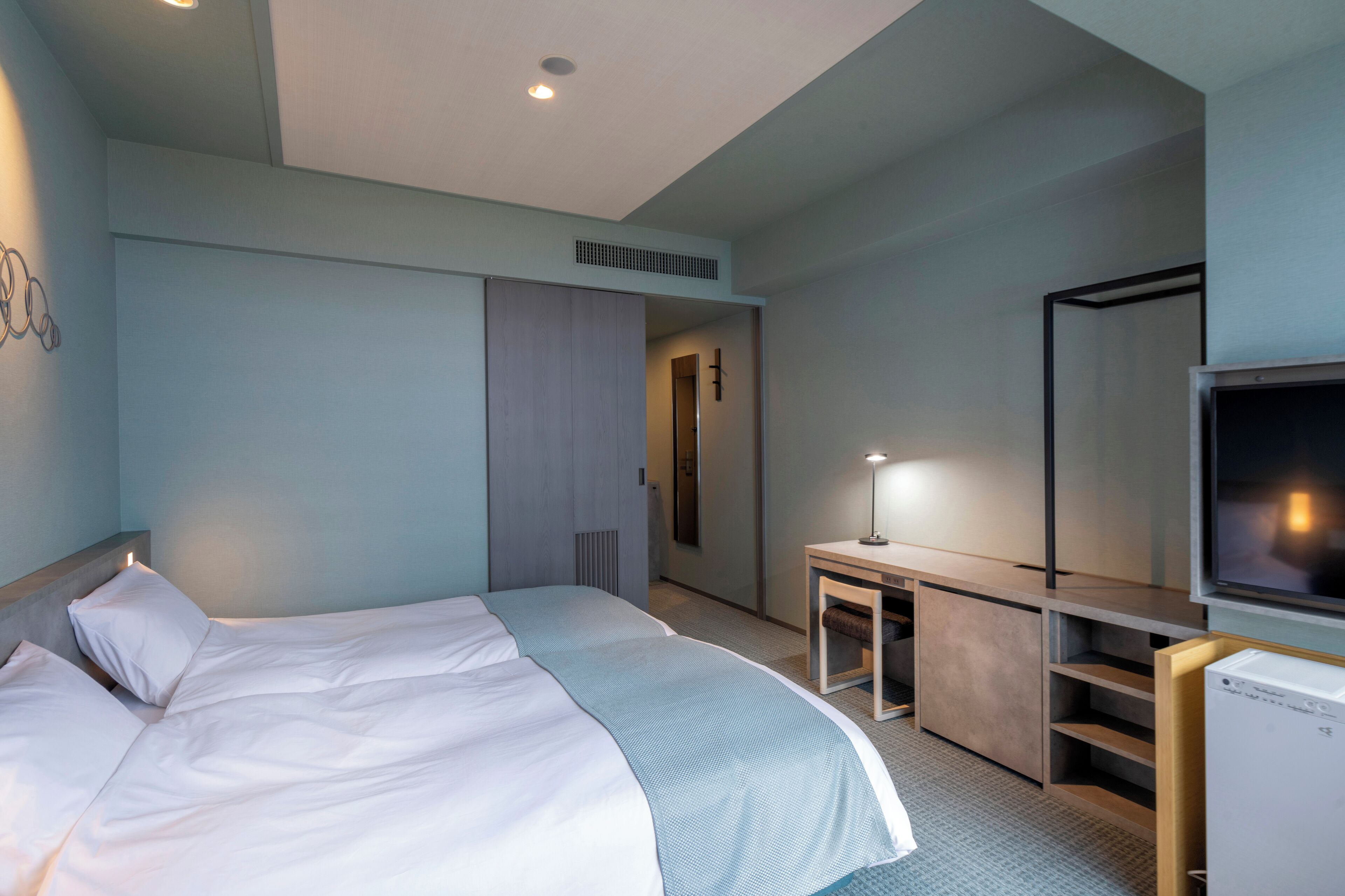 Una habitación de hotel con cama, escritorio con lámpara, televisor y armario.