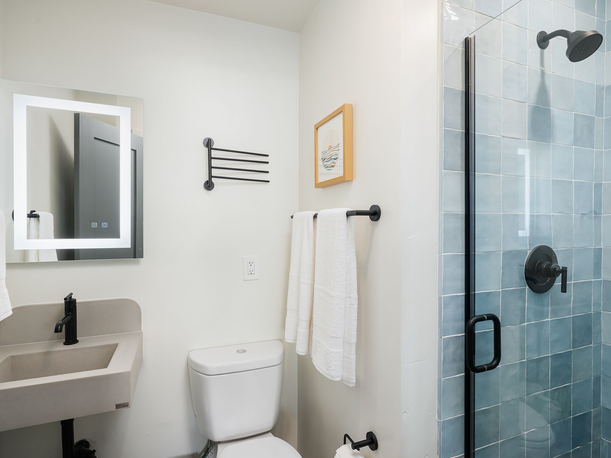 Un baño moderno con lavamanos blanco, inodoro, cabina de ducha de vidrio y toallero de pared.