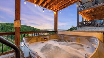 Een hottub met een houten terras, uitzicht op het landschap en een balkon met buitenmeubels.