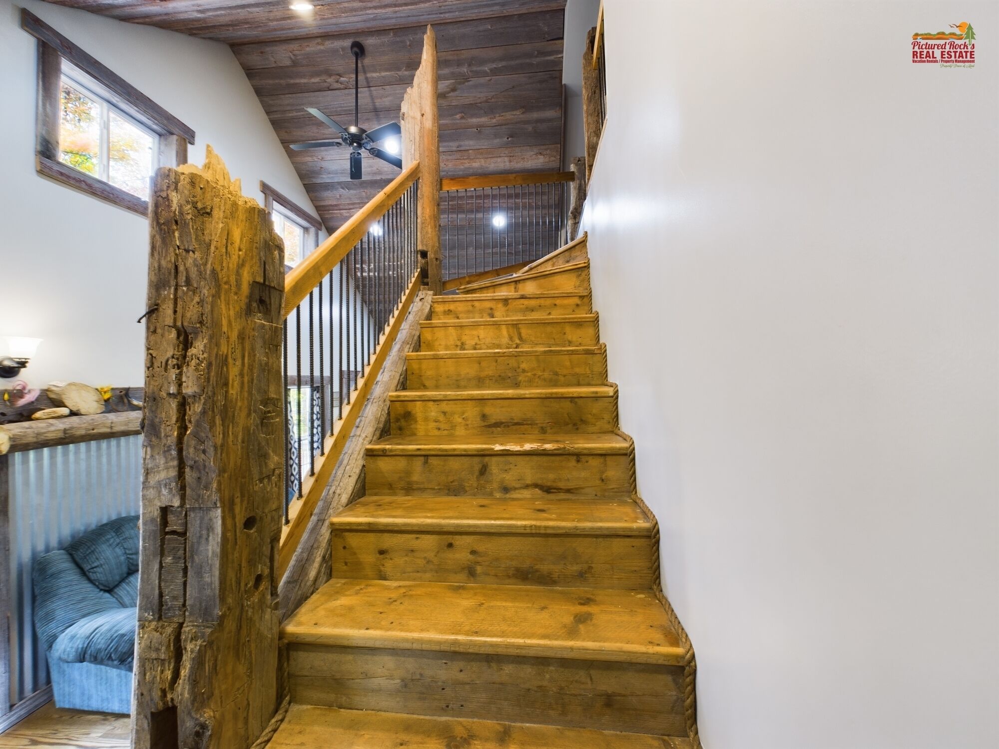 A wooden staircase with a handrail, a ceiling fan, and a window with blinds.
