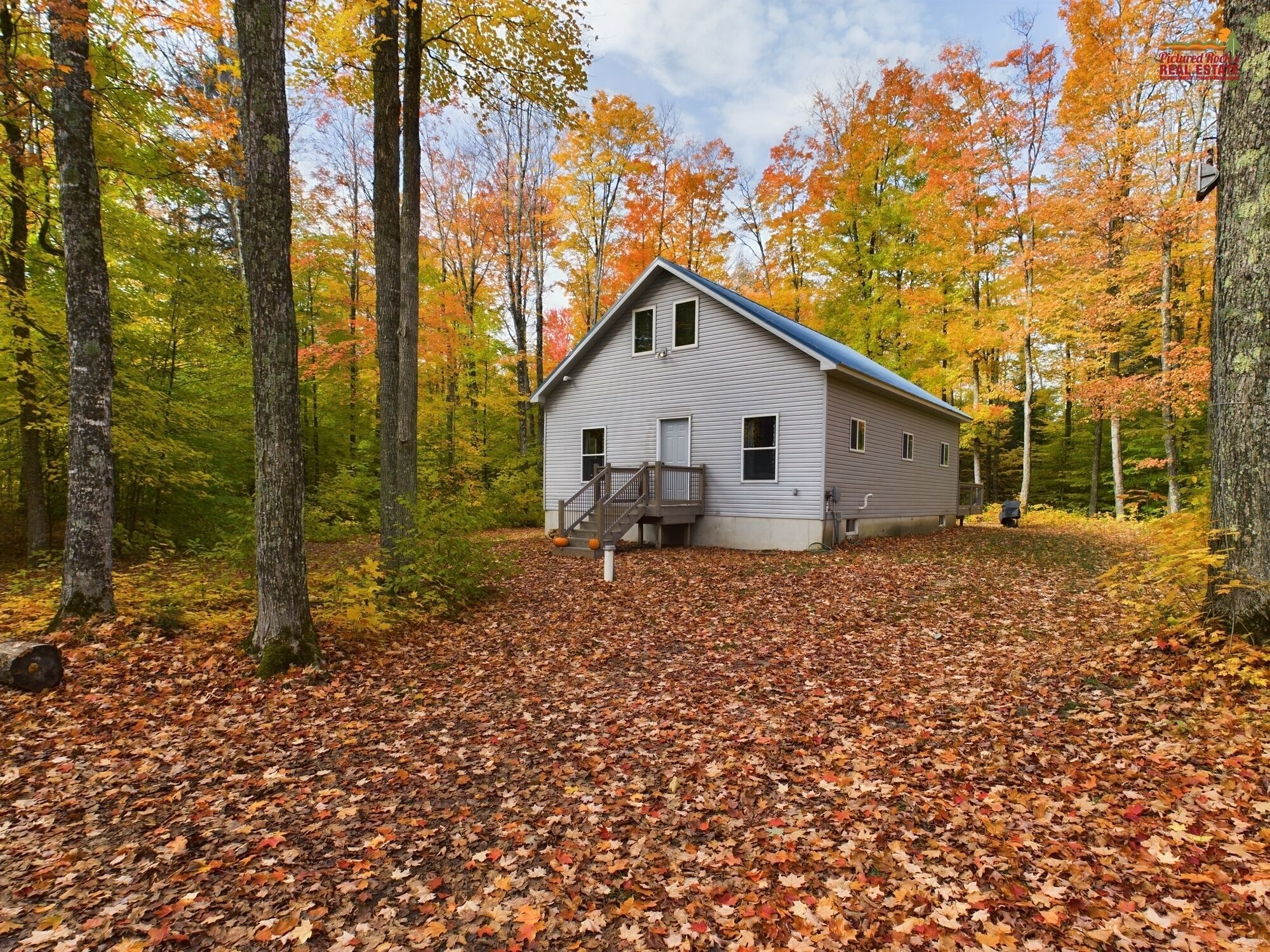 A cabin with a front porch and a staircase, surrounded by a forest with autumn-colored leaves.