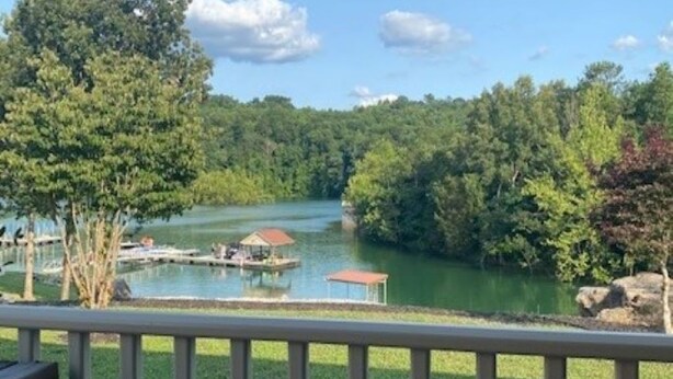 A view from a balcony overlooking a lake with a dock and a gazebo, surrounded by trees and a grassy area. - Lakefront Cabin in quiet cove. No steps to private boat slip. Pet friendly. (Jacksboro)