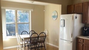 A kitchen with wooden cabinets, a white refrigerator, and a dining area with a table and chairs. - Lakefront Cabin in quiet cove. No steps to private boat slip. Pet friendly. (Jacksboro)