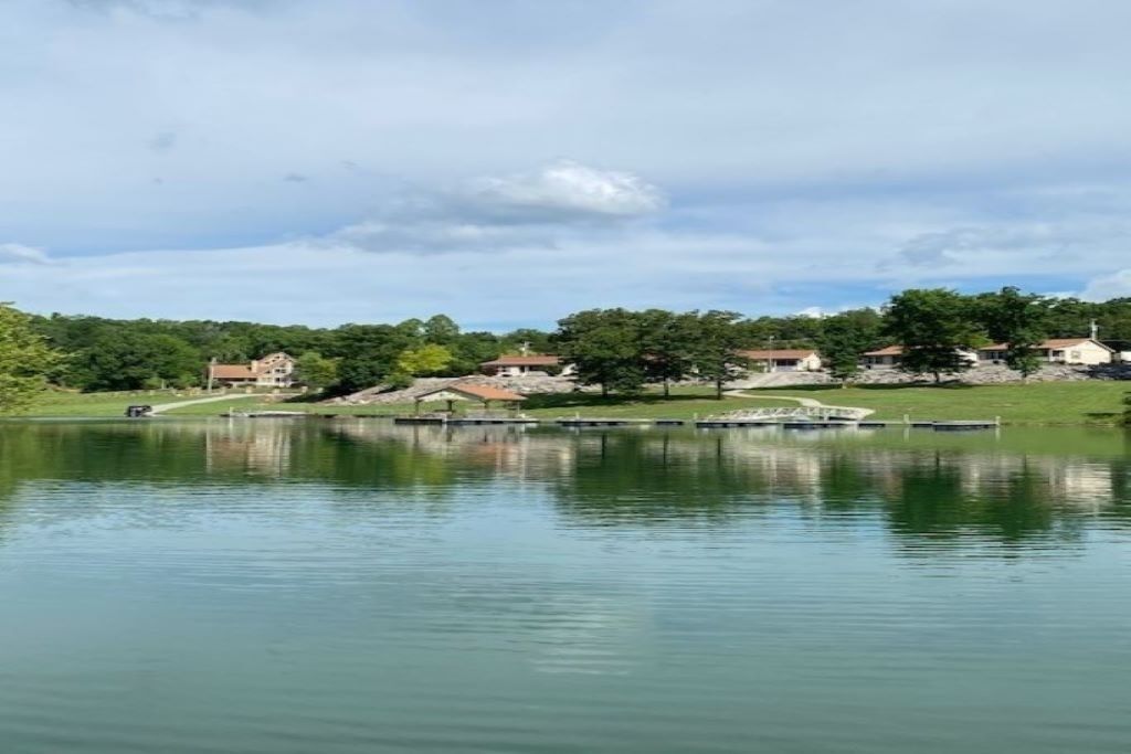 Un lago tranquilo con un muelle y casas al fondo.