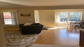 A living room with a dark-colored sofa, a patterned rug, and a dining area with a table and chairs. - Lakefront Cabin in quiet cove. No steps to private boat slip. Pet friendly. (Jacksboro)