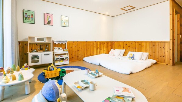 Una habitación moderna y bien iluminada con una pared de madera, una cama blanca, un área de cocina y una mesa de juegos con juguetes.