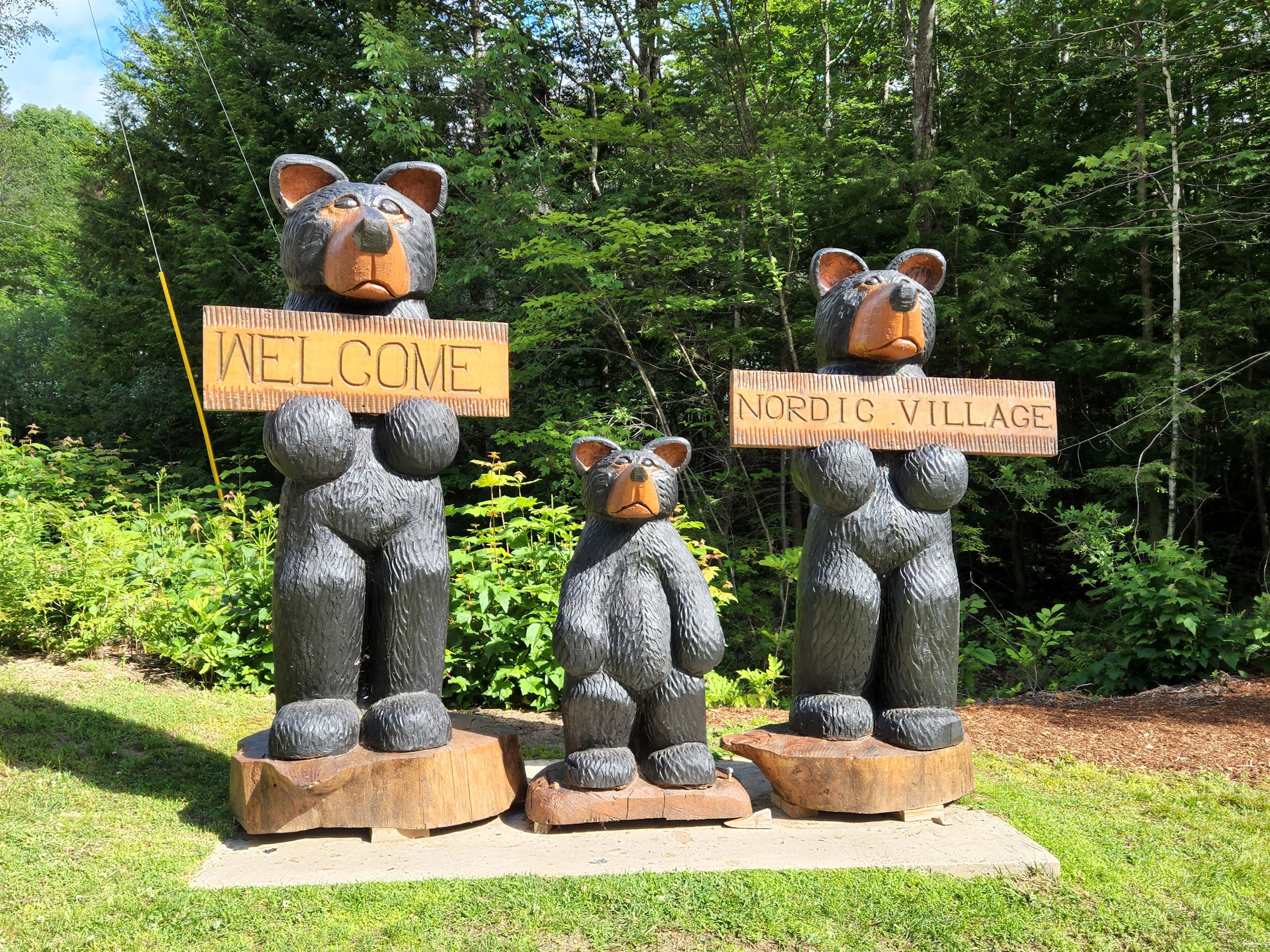 Trois statues d’ours tenant des panneaux sur lesquels on peut lire « BIENVENUE » et « VILLAGE NORDIQUE ».