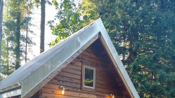 A small wooden cabin with a pitched roof, a covered porch with two chairs, and a small table.