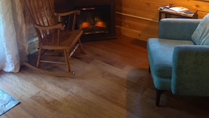 A cozy cabin interior with a wooden interior, a fireplace, a television mounted on the wall, and a window with a view of greenery.