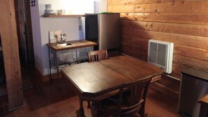 A compact kitchen with wooden walls, a sink, a refrigerator, and a dining table with chairs.