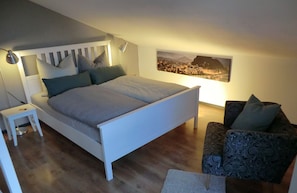 Een slaapkamer met een bed, nachtkastje, lamp en een stadsgezichtschilderij aan de muur.