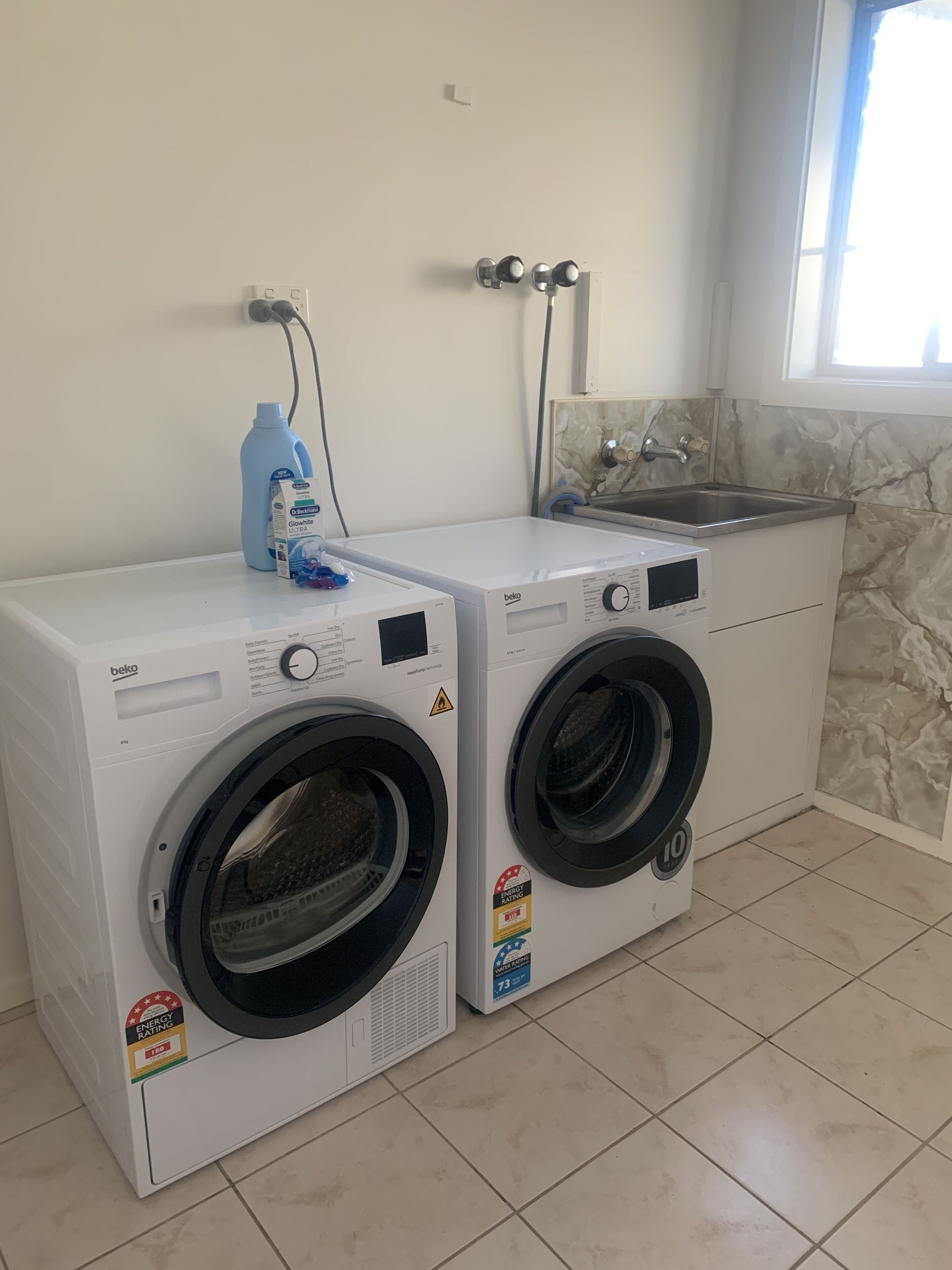 Deux machines à laver à chargement frontal, équipées d’un tuyau d’arrivée d’eau et d’un robinet fixé au mur.