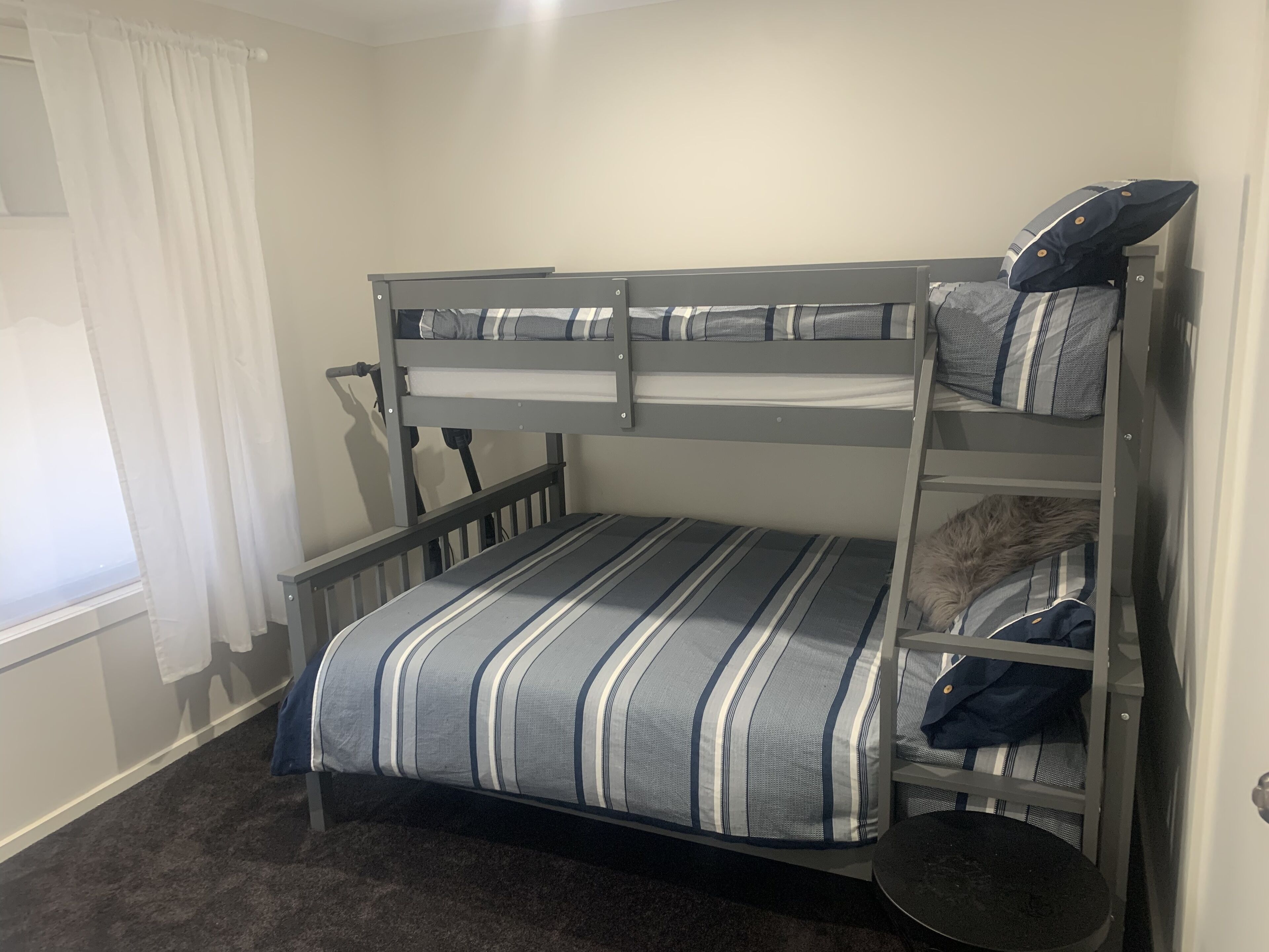 A bunk bed with striped bedding, a small round table, and a window with curtains.