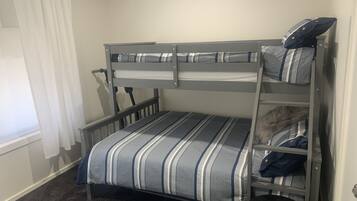 A bunk bed with striped bedding, a small round table, and a window with curtains.