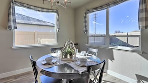 A dining area with a round table, chairs, and a chandelier. There are windows with curtains, and a view of a fence and sky. - Family-Friendly Grand Junction House w/ Patio (Grand Junction)