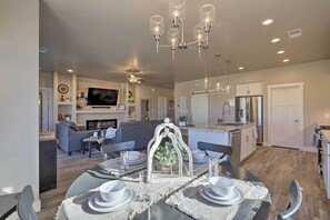 Una cocina moderna con una isla central, un comedor con candelabro y una sala de estar con sofá y televisor.