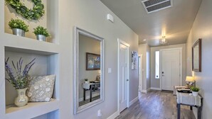 A hallway with a wooden floor, a mirror, and a door. There are potted plants on a shelf and a table with a lamp. - Family-Friendly Grand Junction House w/ Patio (Grand Junction)